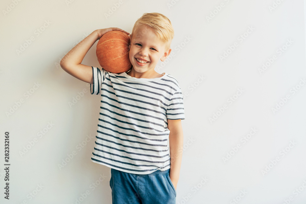 Happy caucasian boy in a striped T-shirt laughs and holds a big ripe pumpkin. Happy caucasian boy in a striped T-shirt laughs and holds a big ripe pumpkin.