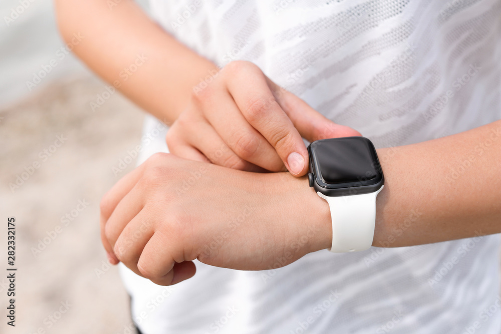 Young woman checking pulse with smartwatch after training outdoors, closeup