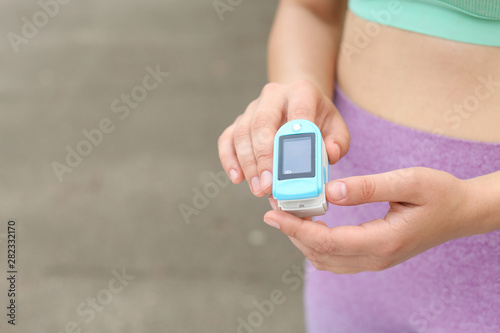 Young woman checking pulse with medical device after training on street, closeup. Space for text