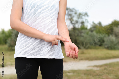 Young woman checking pulse after training in park, closeup