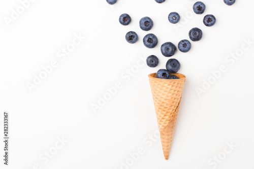 Ice cream cone filled with .blueberries on a white background. Berries fall out from a waffle cone.