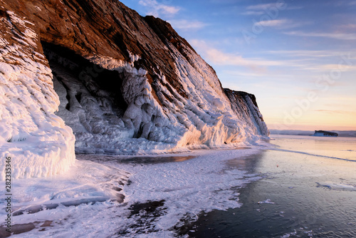 Lake Baikal is covered with ice and snow, strong cold, thick clear blue ice. Icicles hang from the rocks. Lake Baikal is a frosty winter day. Amazing place