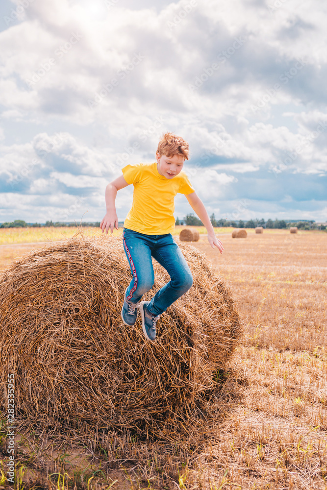Red-haired Caucasian boy indulges on a farm field jumping from a haystack Red-haired Caucasian boy indulges on a farm field jumping from a haystack