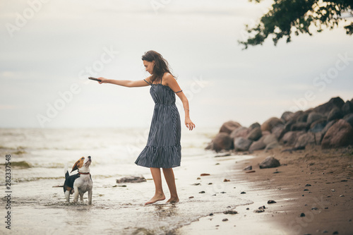 Image of happy woman 20s hugging her dog while walking along the beach © Alexandr