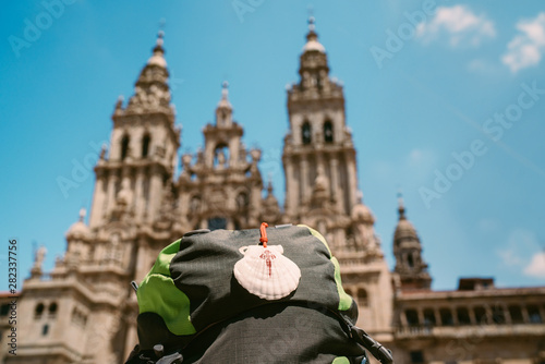 Pilgrim's backpack with famous pilgrims' mascot and sign seashell with Cross of Saint James at  on the Obradeiro square (plaza) - the main square in Santiago de Compostela with Catedral de Santiago. photo