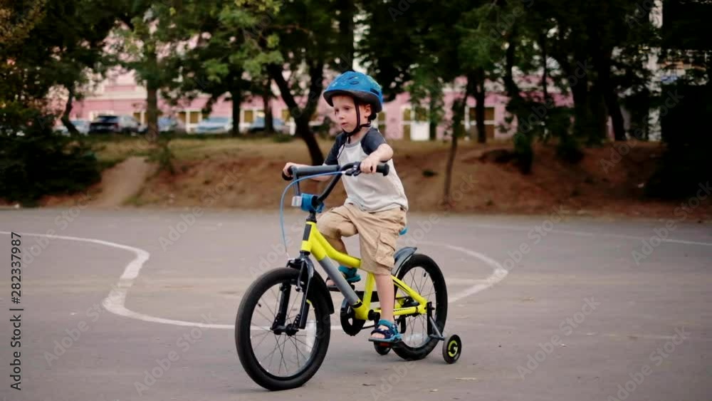 Child riding bicycle in park at sunset light. Kid in helmet learning to ride at summer. Happy boy riding bike, having fun outdoors on nature. Active sport family leisure. Healthy holidays. Slow motion Child riding bicycle in park at sunset light. Kid in helmet learning to ride at summer. Happy boy riding bike, having fun outdoors on nature. Active sport family leisure. Healthy holidays. Slow motion