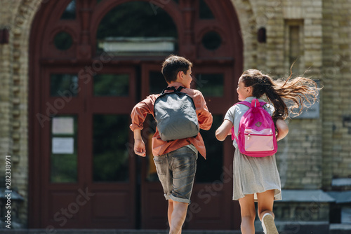Canvas Print back view of two schoolkids with backpacks running in schoolyard