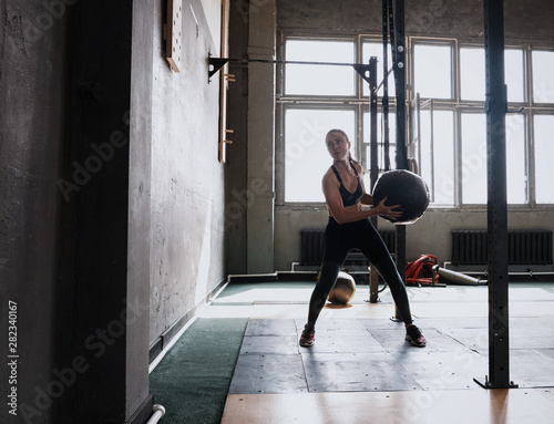 Woman doing exercise with heavy medicine ball in gym.