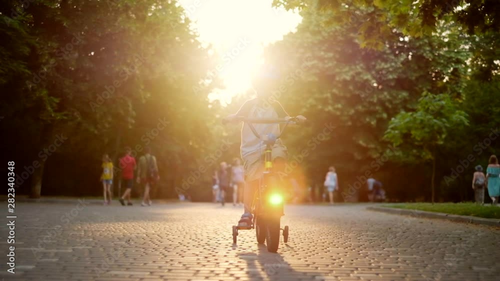 Child riding bicycle in park at sunset light. Kid in helmet learning to ride at summer. Happy boy riding bike, having fun outdoors on nature. Active sport family leisure. Healthy holidays. Slow motion