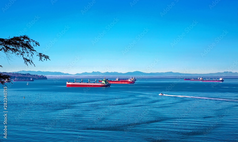 Obraz premium Vancouver harbor, ocean tankers waiting for loading in port white waves in a sunny day on the background scenery of blue sky and mountain range