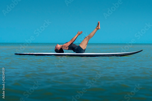 Woman does yoga, uttana padasana position, on paddleboard in the water photo