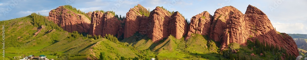 Landscape with red mountains and rocks, green hills, blue sky, panorama