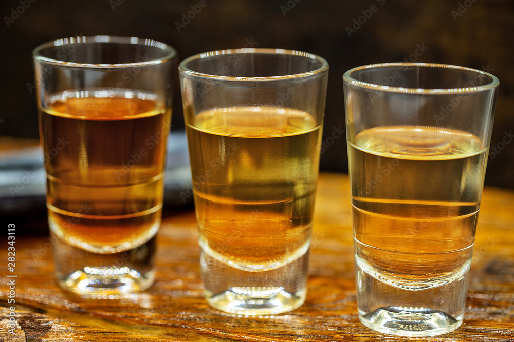 Several glasses of brazilian cachaça isolated on rustic wooden background, variations and types of brazil cachaça, typical drink from brazil.