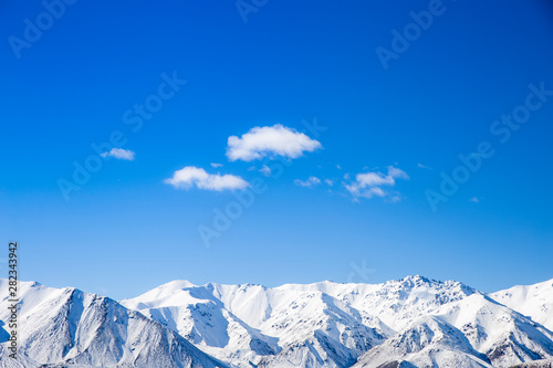 Fototapeta Naklejka Na Ścianę i Meble -  Mountain peaks snow covered mountain range with blue sky and clouds