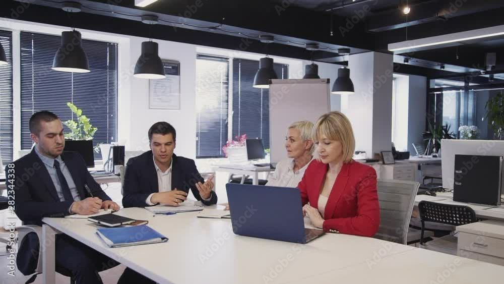 Team of four confident businessperson sitting together inside workspace office with modern loft interior. Two man and two smart woman talking about innovation or investments in new startup Team of four confident businessperson sitting together inside workspace office with modern loft interior. Two man and two smart woman talking about innovation or investments in new startup