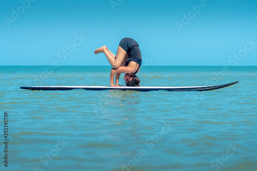 Woman does yoga on paddleboard at sea, Intermediate posture to reach sirsasana photo