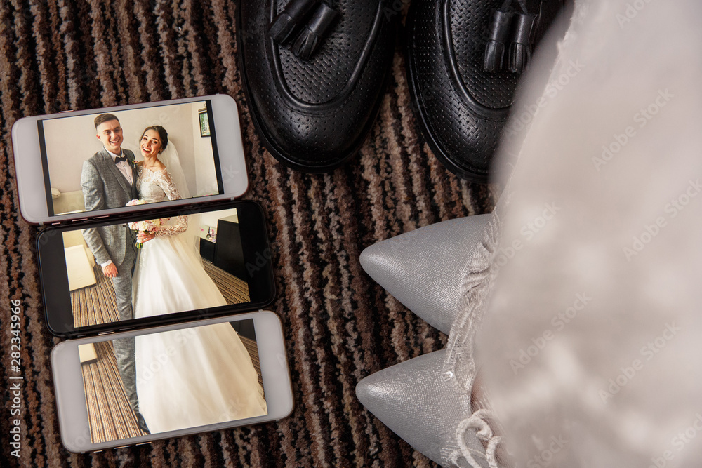 Creative wedding photo. Portrait of bride and groom on the screen of three smartphones near bridal shoes and groom's shoes Creative wedding photo. Portrait of bride and groom on the screen of three smartphones near bridal shoes and groom's shoes
