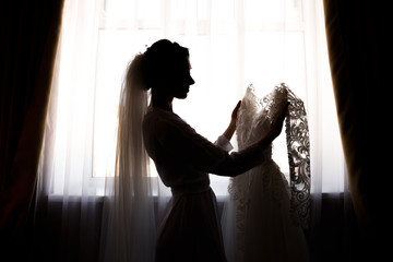 Bride holding white wedding dress with lace, embroidery. Bride getting ready