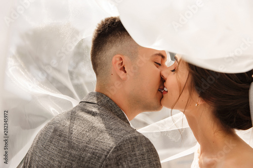 Bride and groom kissing in white bridal veil at wedding day