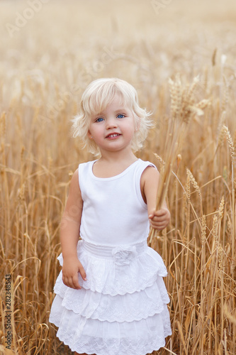 Portrait of handsome blond girl with blue eyes, face close up at summer time, in the wheat field. Cute little girl in the summer field of wheat. A child with a bouquet of wheat in his hands