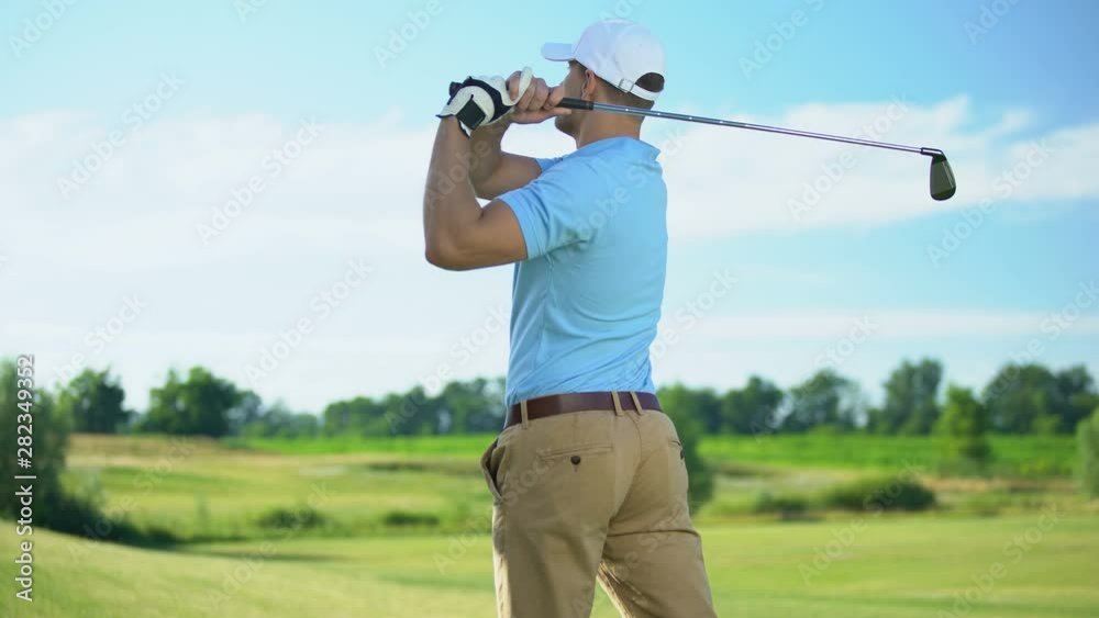 Experienced golf player hitting ball in draw position at course, back view Experienced golf player hitting ball in draw position at course, back view