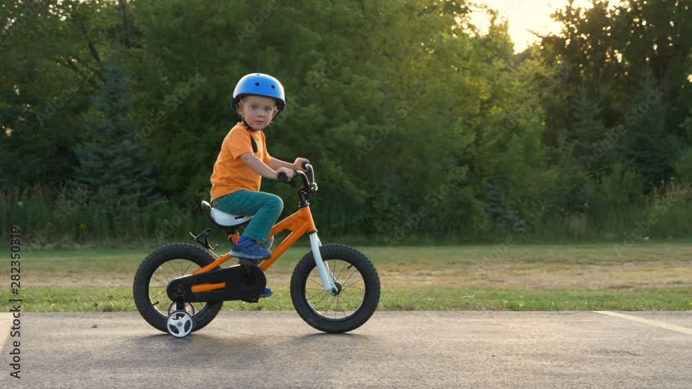 Cute little boy ( two years old child) is riding bike. Kid in orange t-shirt and blue helmet. Orange kids bicycle. First experience, childhood memories Cute little boy ( two years old child) is riding bike. Kid in orange t-shirt and blue helmet. Orange kids bicycle. First experience, childhood memories