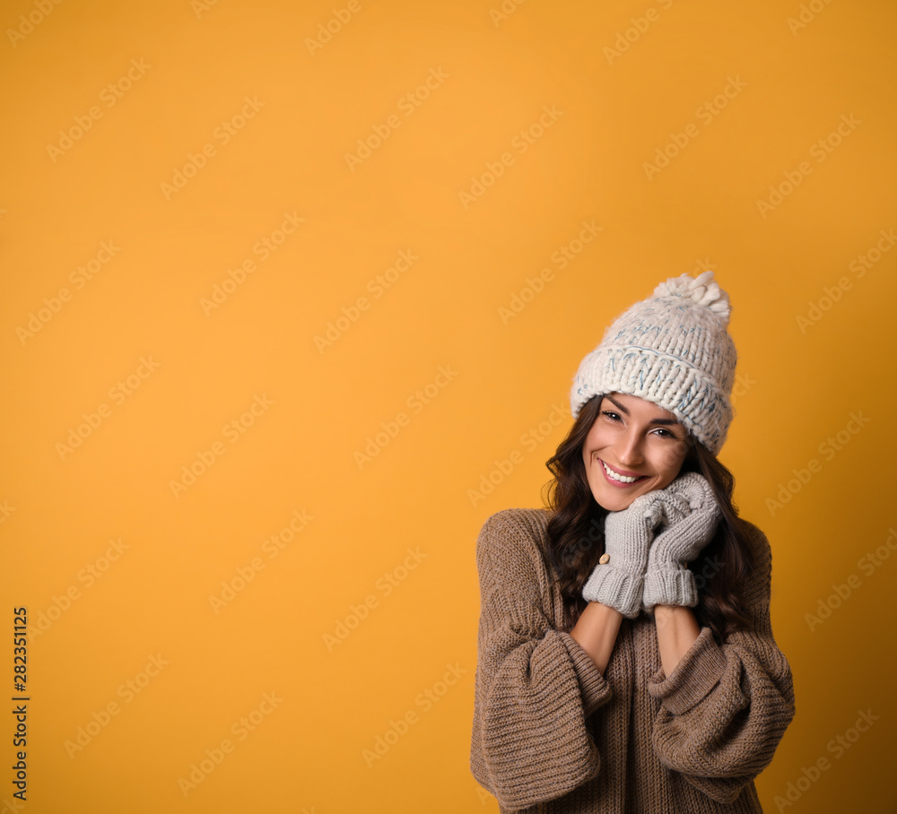Young woman in warm sweater, hat and mittens on yellow background, space for text. Christmas season Young woman in warm sweater, hat and mittens on yellow background, space for text. Christmas season