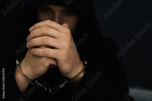 Man detained in handcuffs against dark background. Criminal law