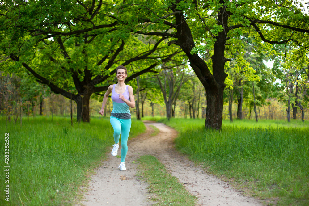 Sports brunette girl jogging in the park. Green forest on the background Sports brunette girl jogging in the park. Green forest on the background