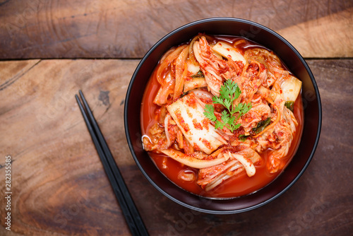 Kimchi cabbage in a bowl with chopsticks on wooden background, Korean food, top view