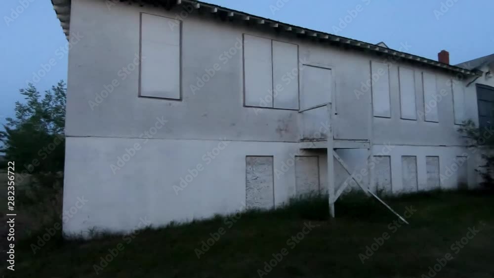 Old abandoned white hospital with boarded up windows and doors after the sunny has gone down.. Old abandoned white hospital with boarded up windows and doors after the sunny has gone down..