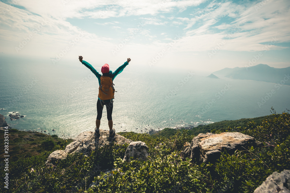 Successful hiker outstretched arms at seaside mountain top cliff edge