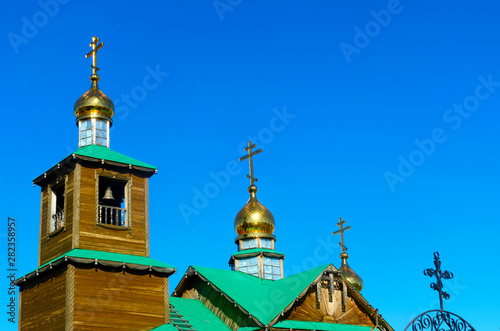 Three Golden domes with a cross of the Orthodox Church made of wood with a green roof and Yakut patterns in the Northern village against the blue sky. photo