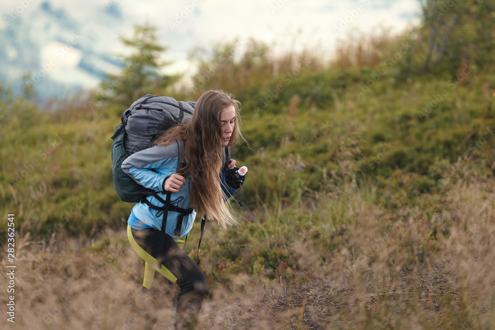 Young woman hiker trekking in mountains. Traveling girl with backpack going along the trail in the mountains. Young woman hiker trekking in mountains. Traveling girl with backpack going along the trail in the mountains.