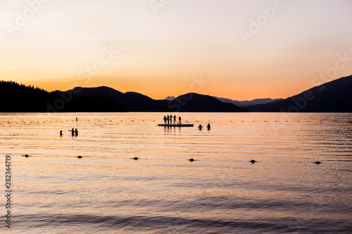 Silhouettes of people standing on a dock in a lake at sunset