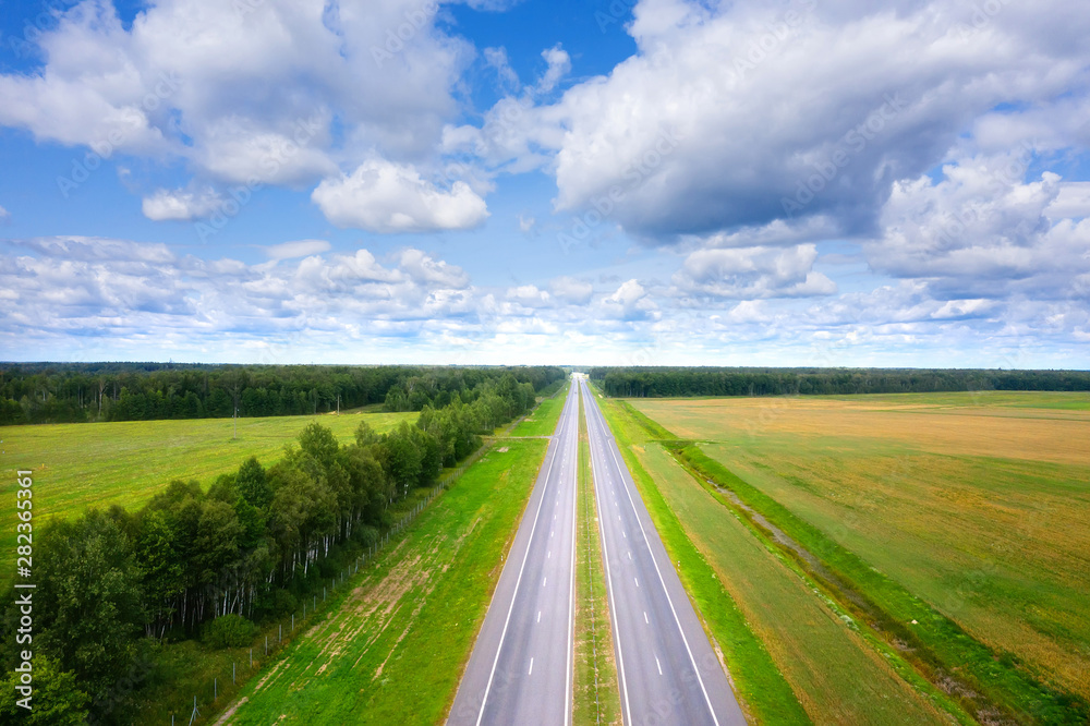 Aerial view of road on sunny summer day. Empty Highway from above. Beautiful landscape of road between green meadow and blue sky with clouds