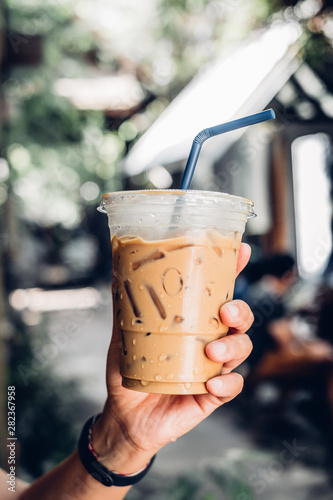 Billede på lærred hand holding iced latte with straw in plastic cup at garden blur cafe restaurant in hot sunny day