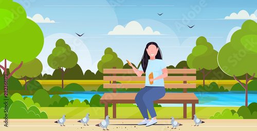 fat obese woman holding bread and feeding flock of pigeon overweight girl sitting wooden bench having fun outdoor public park landscape background flat full length horizontal