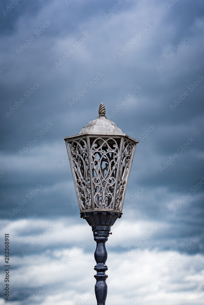 Wrought iron lamps lighting on the background of clouds.