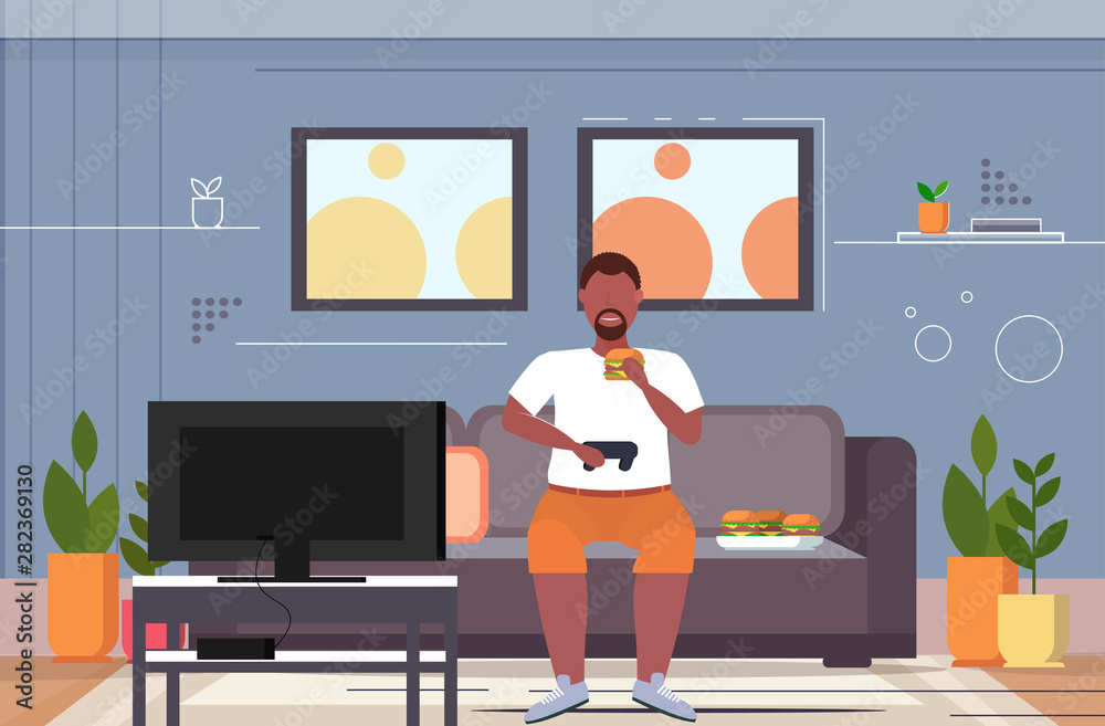 fat obese man sitting on couch eating hamburger using joystick game pad overweight guy plying video games on tv unhealthy lifestyle concept living room interior flat horizontal full length fat obese man sitting on couch eating hamburger using joystick game pad overweight guy plying video games on tv unhealthy lifestyle concept living room interior flat horizontal full length