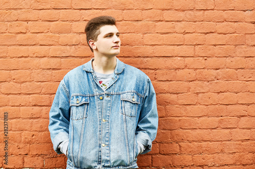 young guy in a denim jacket against a brick wall. copyspace