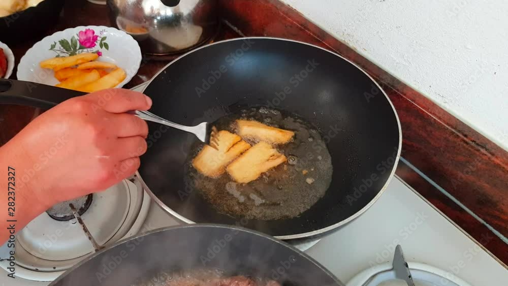 Frying Yuca (Cassava) in pan with oil on stove, golden color, and turning over with fork (Peruvian Food) Frying Yuca (Cassava) in pan with oil on stove, golden color, and turning over with fork (Peruvian Food)