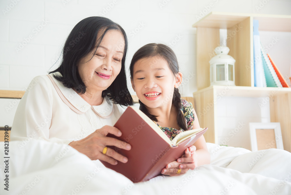 Senior asian woman reading book with granddaughter on bed. Senior asian woman reading book with granddaughter on bed.