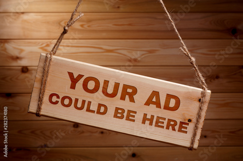 Wooden signboard with the words your ad could be here on a rough rope on a beautiful wooden background