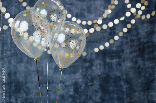 Three balloons with confetti and gold garlands on a smoky dark blue background. Birthday and holiday decor.