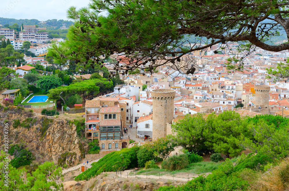 Old tower and stone fortress walls against background of resort town of Tossa de Mar, Costa Brava, Spain