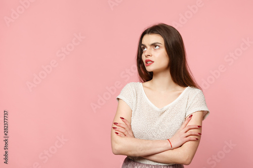Preoccupied puzzled young woman in casual light clothes posing isolated on pastel pink wall background studio portrait. People lifestyle concept. Mock up copy space. Looking up, holding hands crossed.