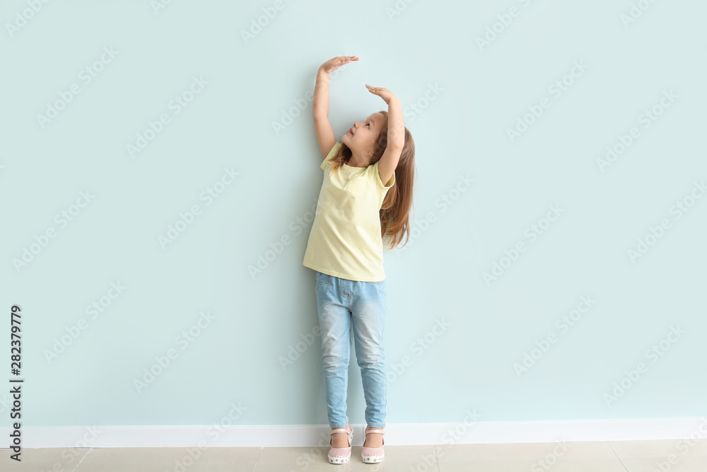 Cute little girl measuring her height near wall - obrazy, fototapety, plakaty 