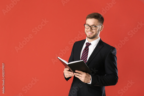 Handsome businessman with book on color background