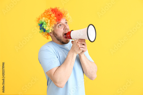 Funny man in wig and with megaphone on color background